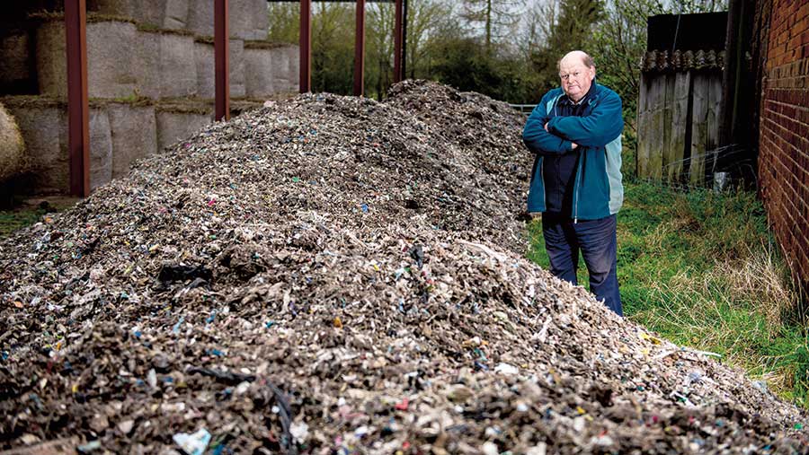 Andrew Nicholls stands next to a huge pile of fly-tipped waste