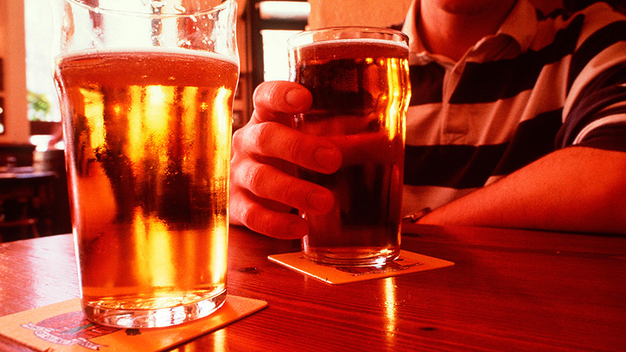 A man holds a pint of lager at a table opposite another pint of beer
