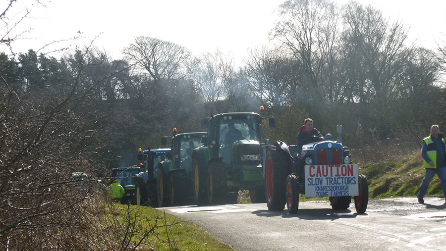 A procession of tractors travel along a road