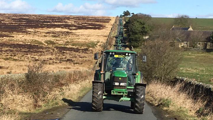 A procession of tractors travels down a hill