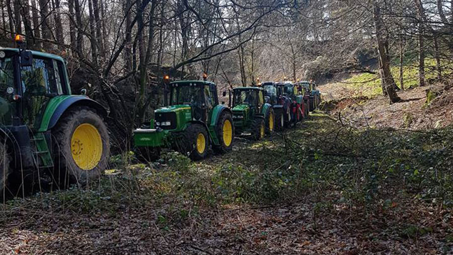 A procession of tractors travels through a wooded area