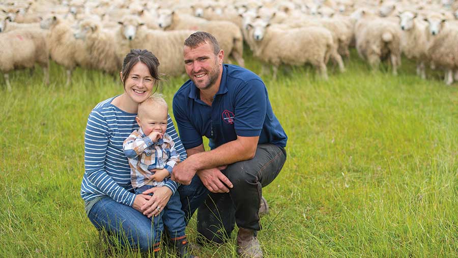 Matt and Pippa Smith stand in a field of sheep with their young son Dusty