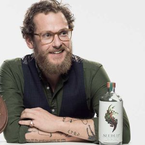 Ben Branson sits with arms folded next to a bottle of Seedlip
