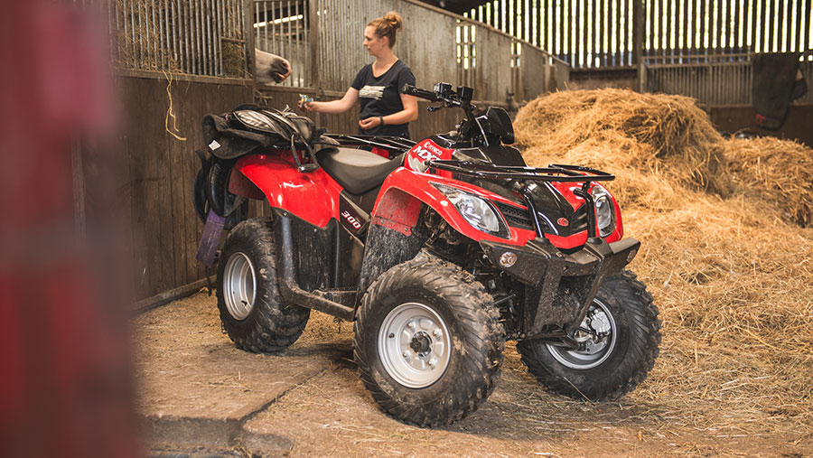 A woman feeds a horse in a barn. In the foreground is a Kymco MXU 300 ATV