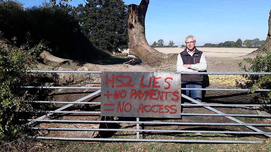 Farmer Tim Burton at a farm gate with a protest sign that reads " HS2 lies + no payments = no access