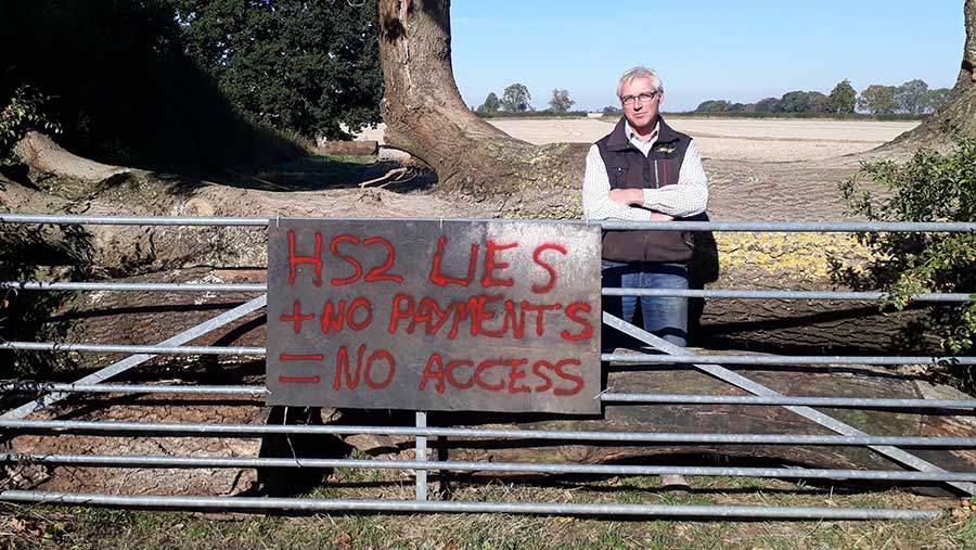 Farmer Sam Burton behing gate with protest sign