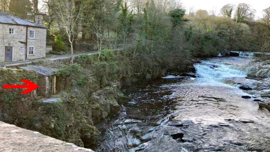 A small toilet building on a rocky river bank