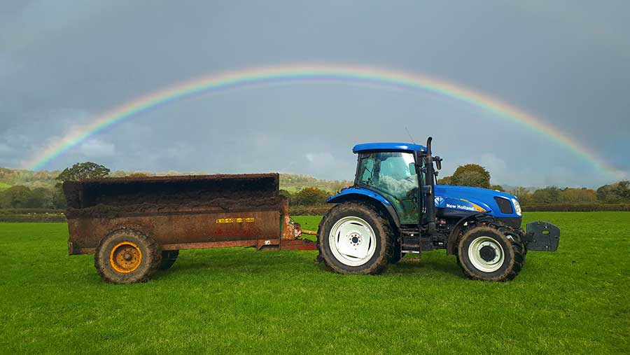 Tractor pulling wagon full of dung with rainbow in the background