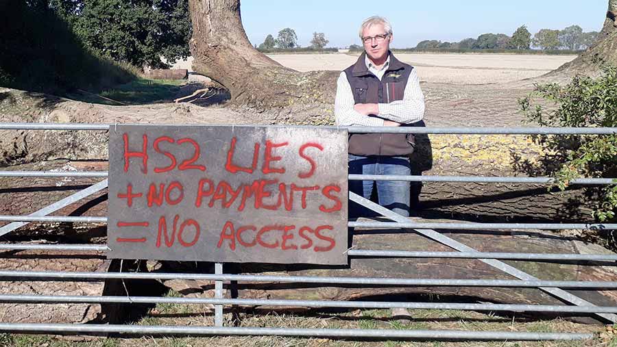 Sam Burton stands beside a sign that says: "HS2 lies + no payments = no access"