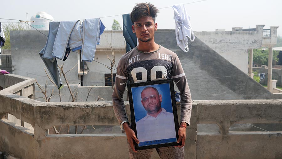 A young Indian man stands with a photograph of his father