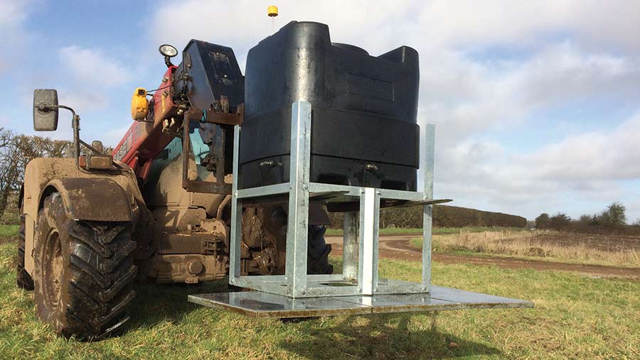 A telehandler moves a black tank with a steel frame