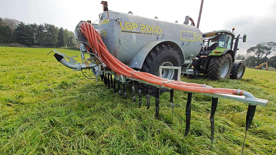 A tractor pulling a slurry tanker with a dribble bar in a field