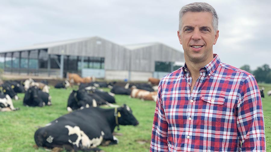 Farmer Phil Kinch stands in a field with cows lying down behind him
