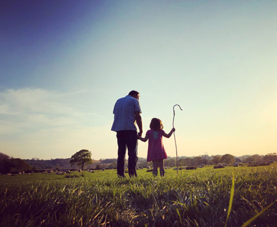 Girl with crook standing with dad in field