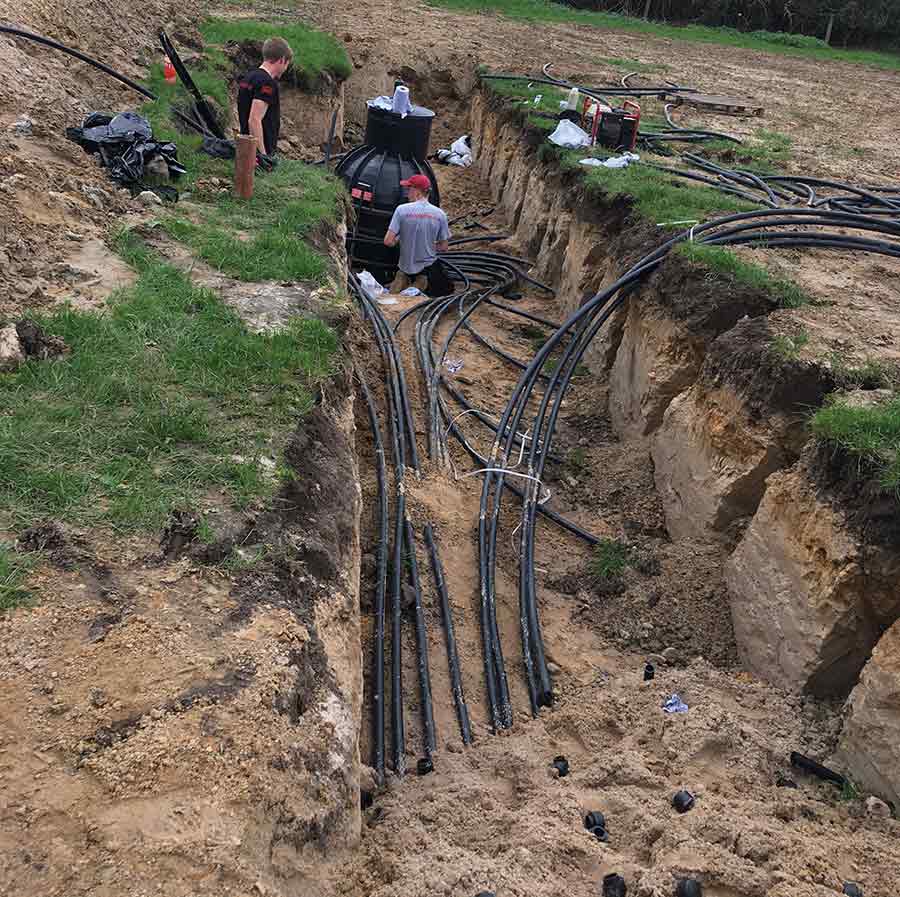 Trench in a field with people laying plastic pipes