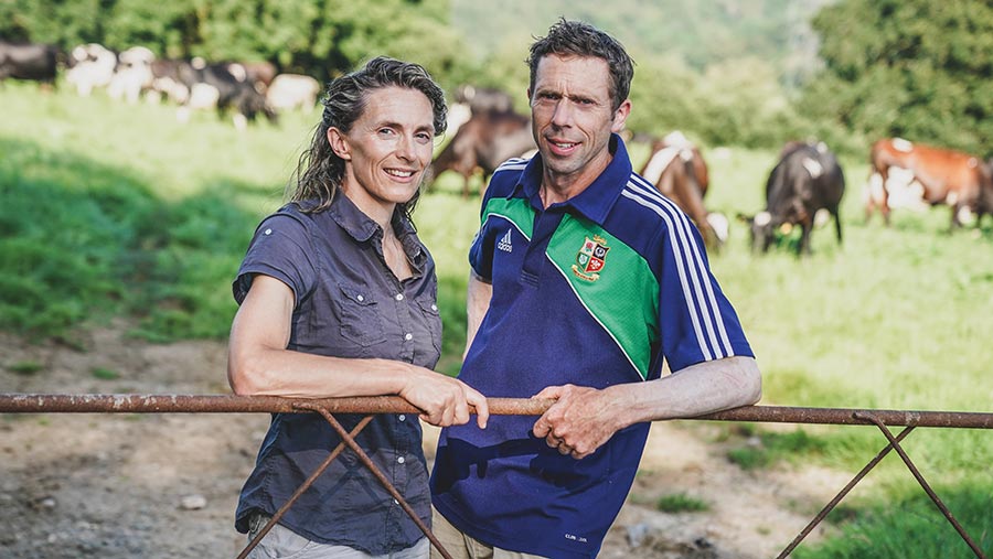 Farming couple lean on a gate with their herd