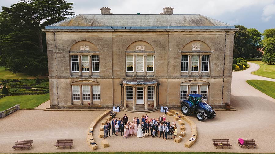 Aerial shot of wedding party outside venue with New Holland tractor