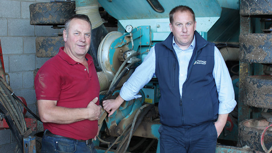 Two men stand with a seed drill