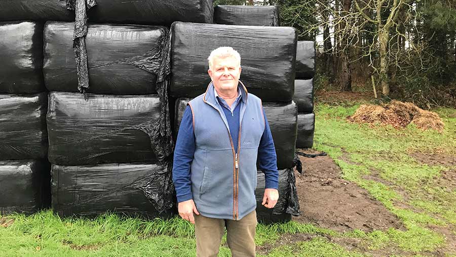 Farmer standinbg in front of plastic-wrapped bales