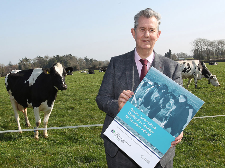 Edwin Poots with poster and cows in the background