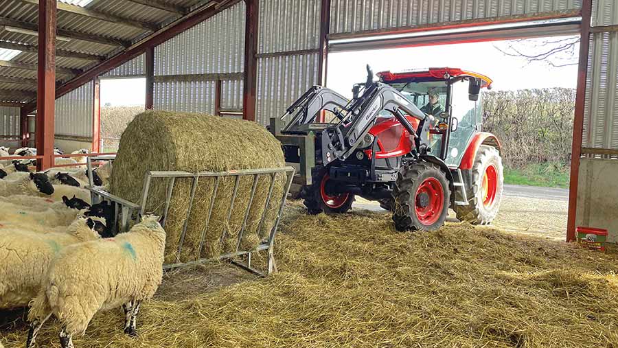 Tractor moving a round bale in a shed