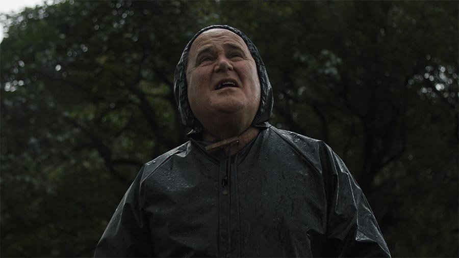 Man wearing wet-weather gear looks up into rain