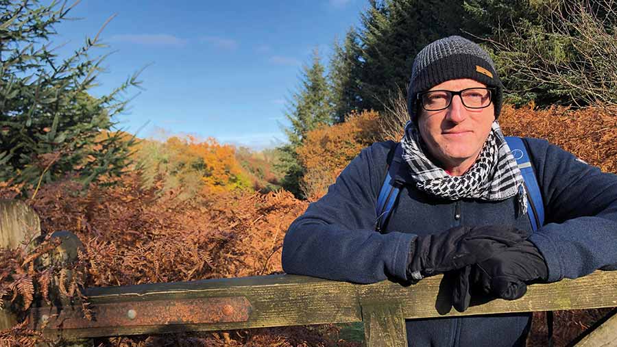 Man leans on a gate with cold weather clothing