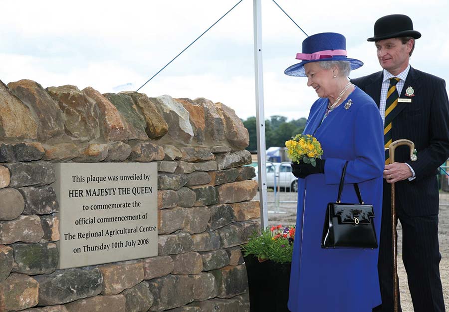 Queen unveils a plaque on a stone wall