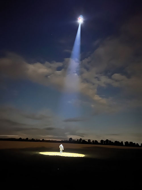 Drone in night sky shining light on someone on the ground