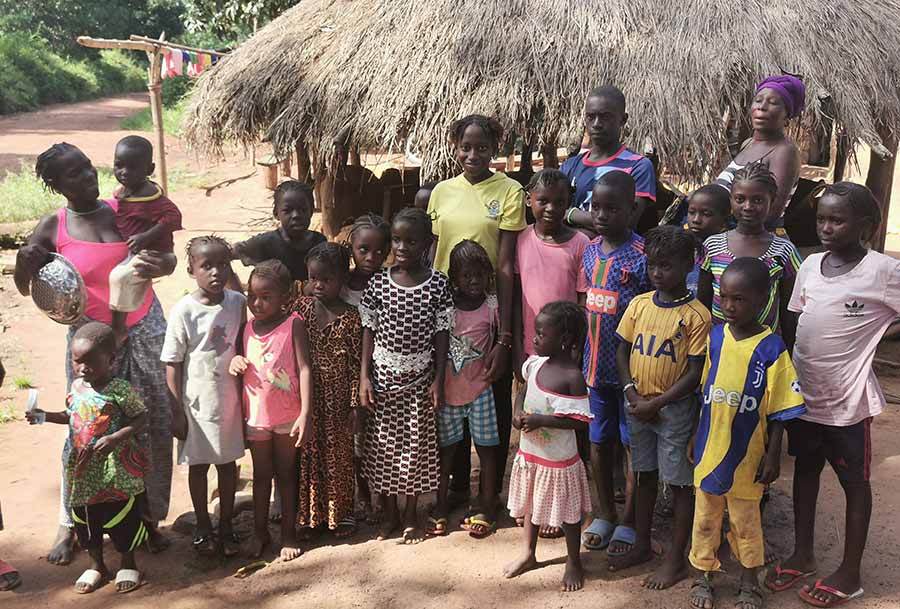 Group of people with lots of children outside a grass-roofed building