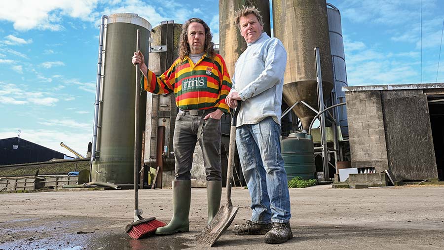 Two men stand in front of feed silos