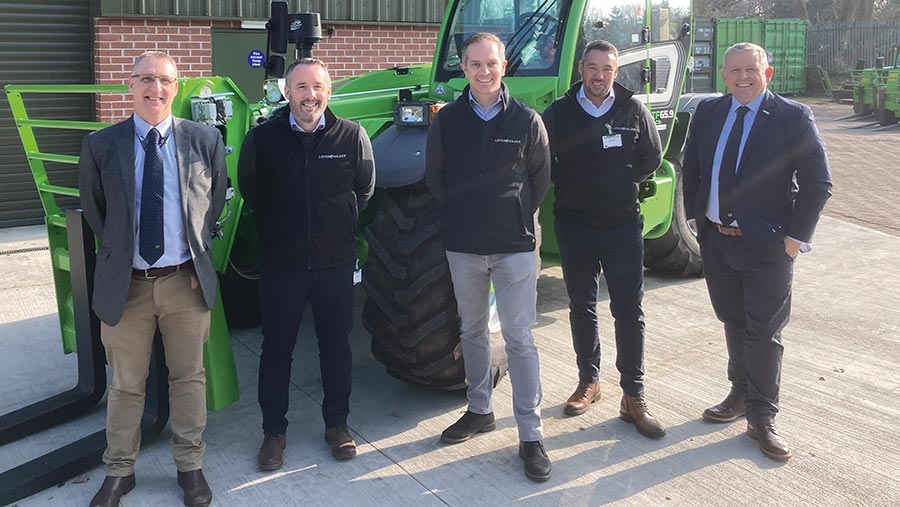 Group of people pose in front of a telehandler