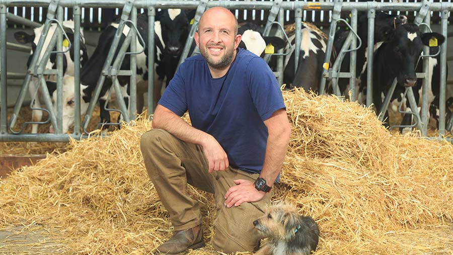 Farmer posing next to a dog and in front of cows and hay