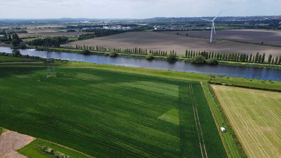 Ariel view of farmland including a wind turbine, trees,  fields and a river flowing down the centre