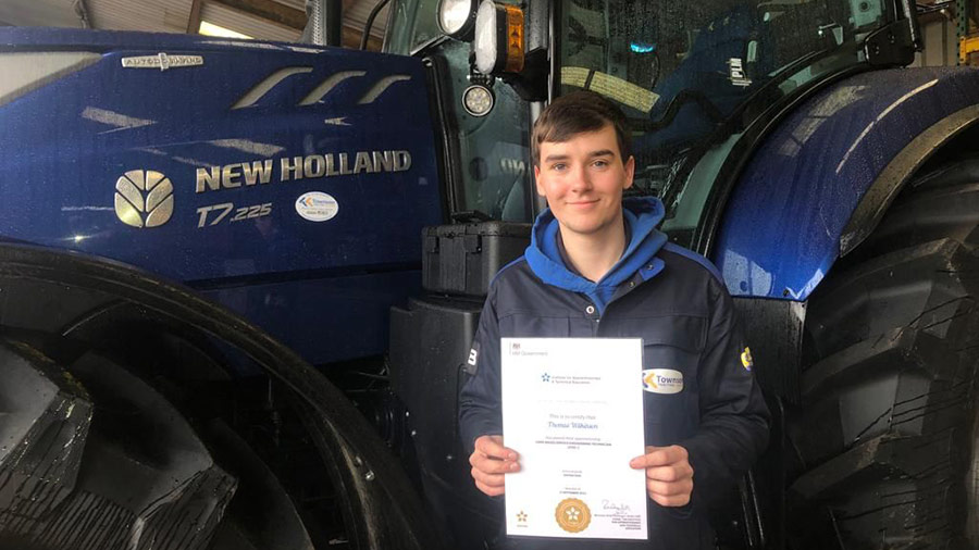 Tom Wilkinson holding his apprenticeship certificate in front of a tractor