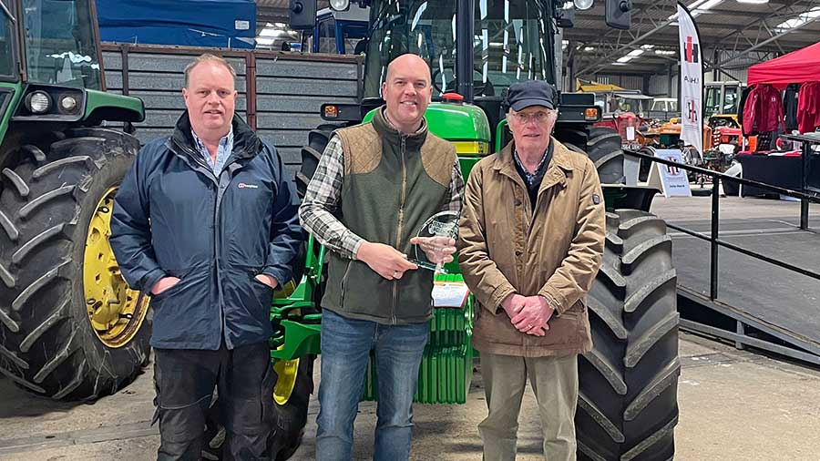 Three men with an trophy standing in front of a tractor