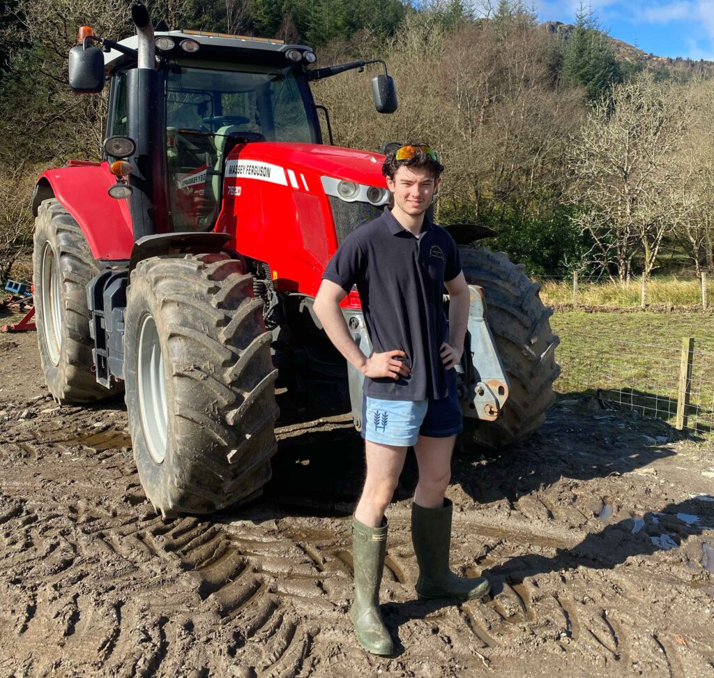 Man in front of a tractor wearing shorts and wellies