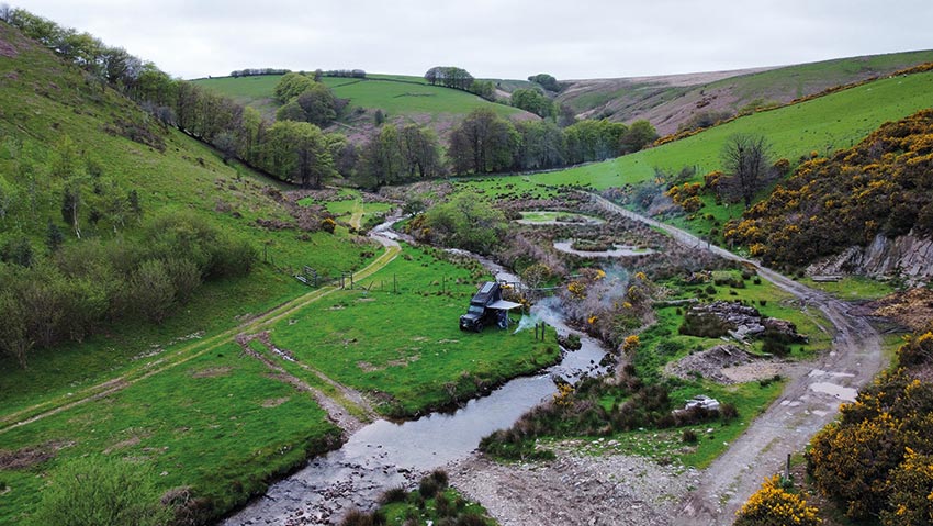 Campervan parked up amongst tree-lined hills and river