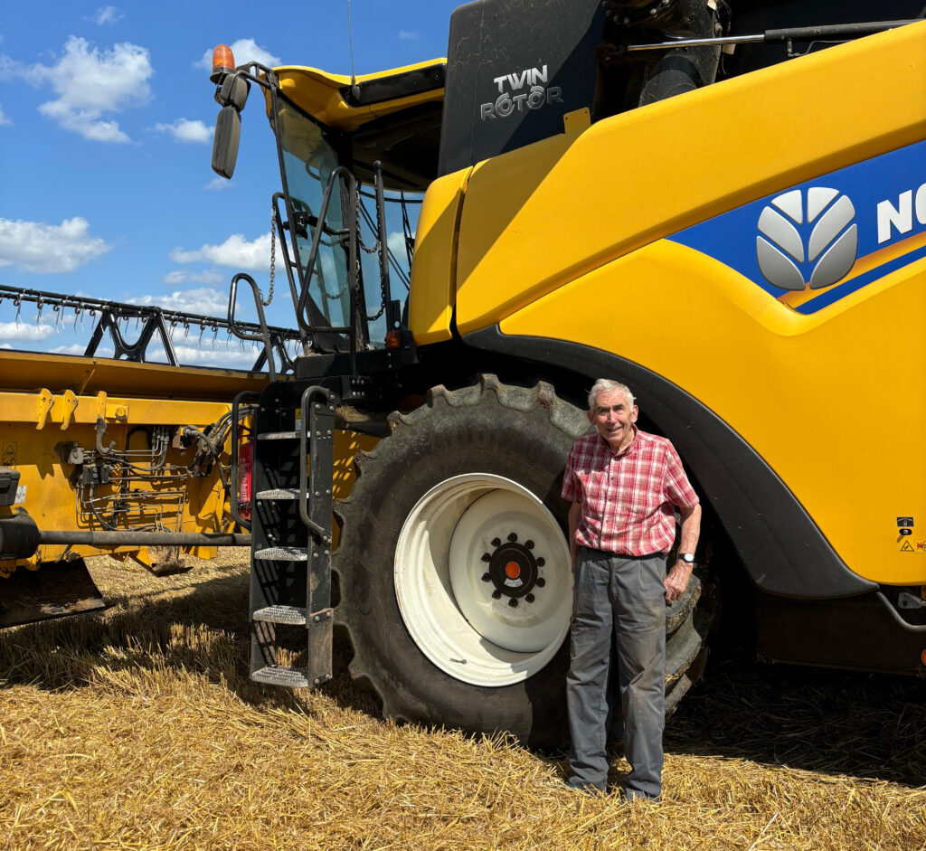 Elederly man stood in front of a combine