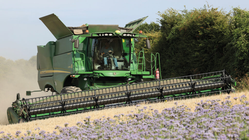 Combine harvester cutting Laureate spring malting barley, with a winter bird food margin of phacelia and other seeds visible