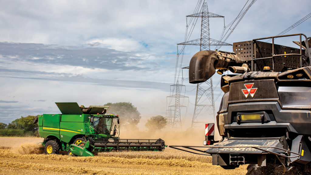 A John Deere S785i and Massey Ferguson 8T cutting a crop of Dawsum winter wheat with pylons visible in the background