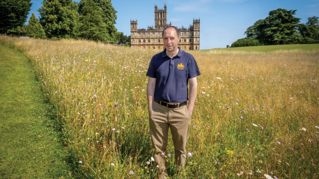 Simon Andrews standing in a wildflower meadow with a large country house in the distance