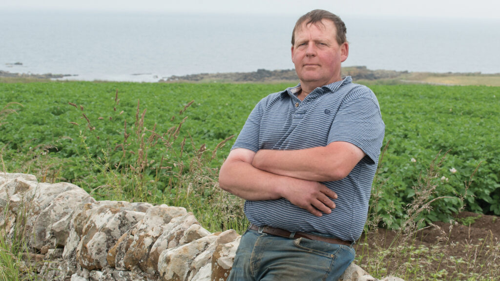 Farmer leaning on a drystone wall on a hillside