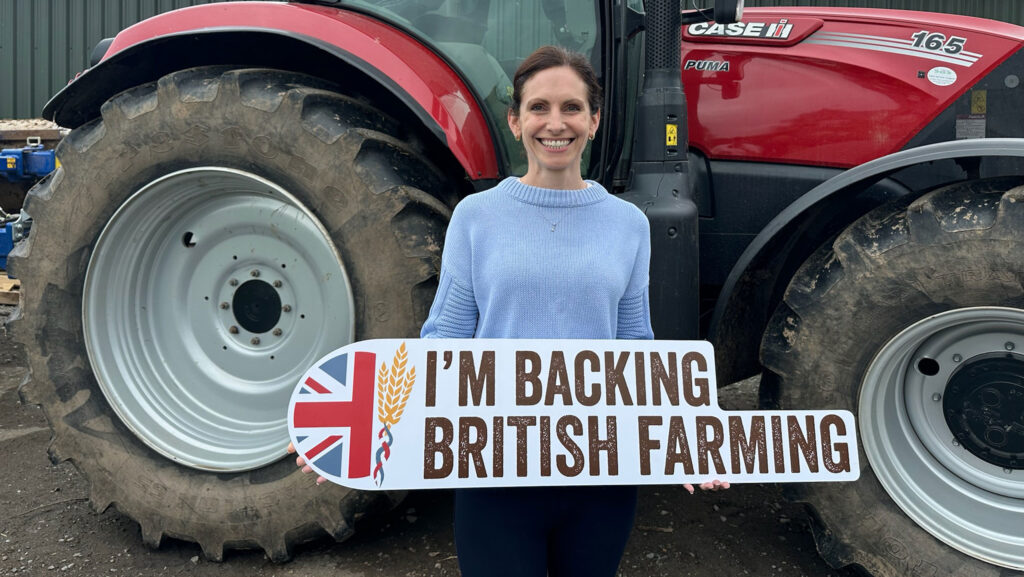 Aphra Brandreth holds placard supporting farmers while standing in front of a tractor