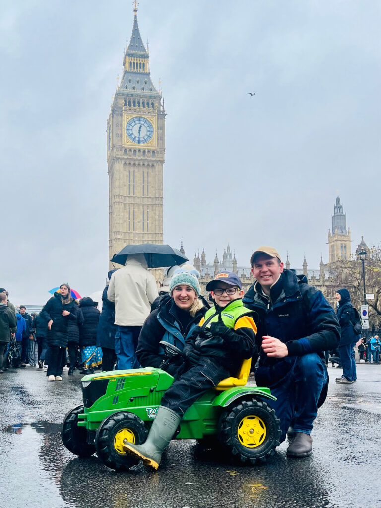 Family at London farming rally, with child riding a toy tractor and Big Ben in the background