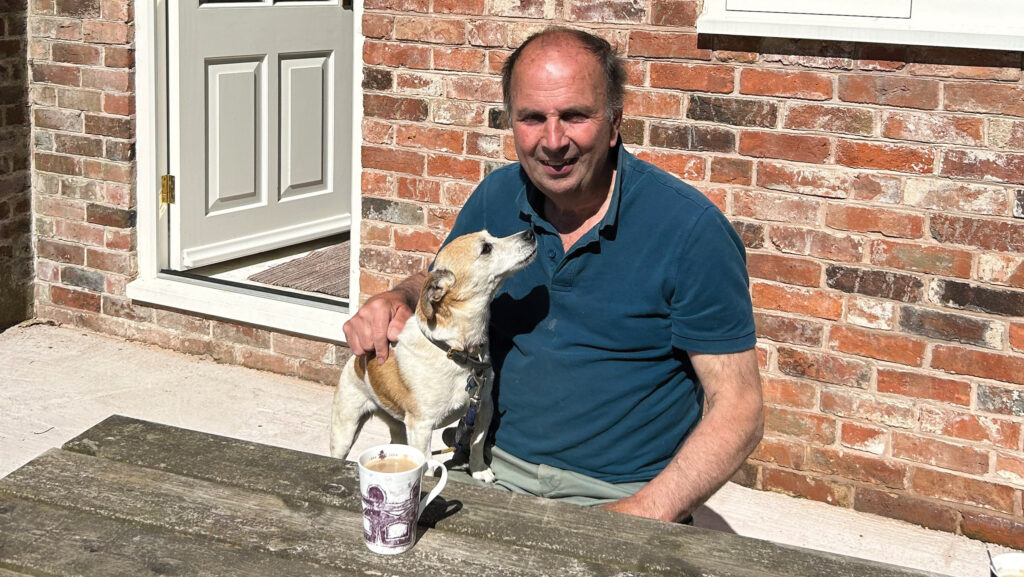 A man having a hot drink at a table with a dog at his side