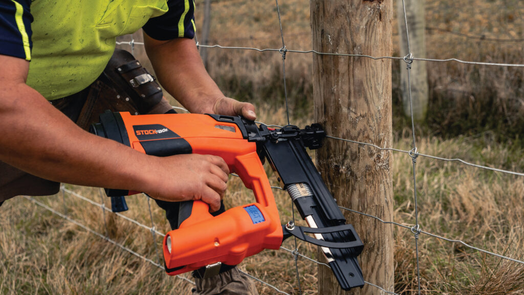 Hands using stapling gun on fence post