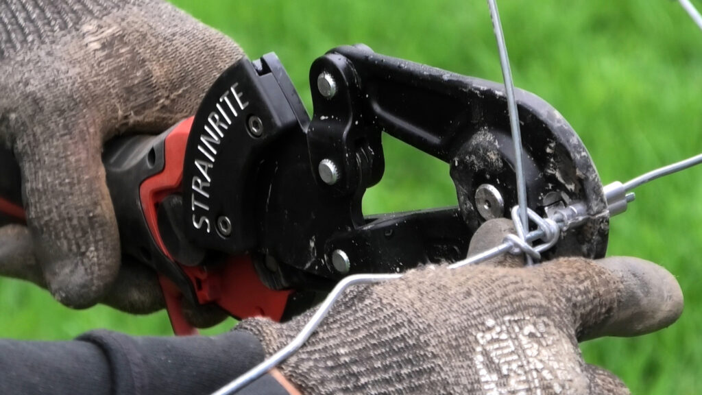 Pair of hands using crimping tool on fence wire