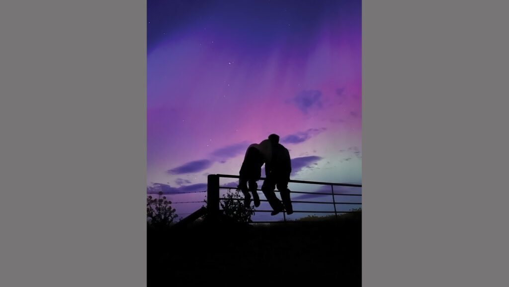 Couple sitting on a fence and watching the Northern Lights