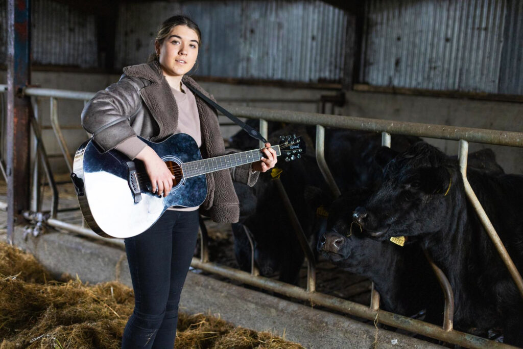 Aviril playing her guitar to heifers in shed